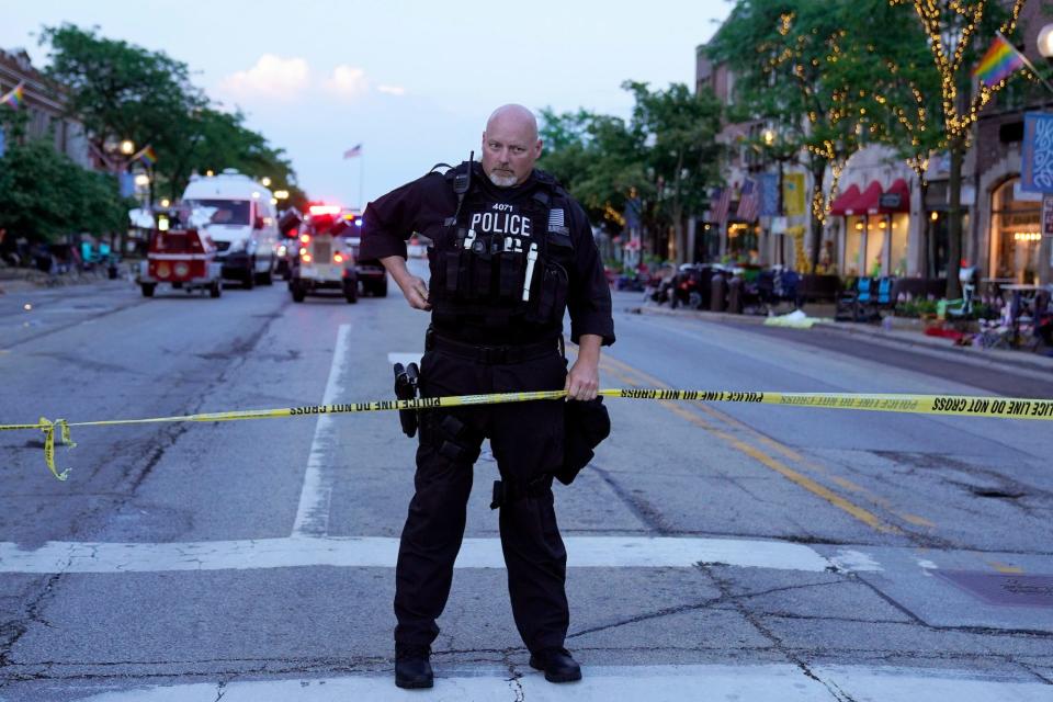 A police officer holds up police tape at the scene of a mass shooting at the Fourth of July parade in downtown Highland Park, a Chicago suburb, on Monday, July 4, 2022.