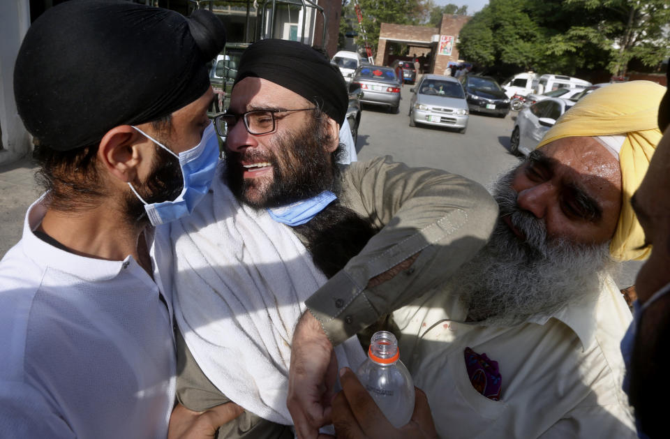 People comfort a man mourning the death of a family member in the bus and train accident, at a hospital in Sheikhupura near Lahore, Pakistan, Friday, July 3, 2020. A passenger train crashed into a bus carrying Sikh pilgrims at an unmanned railway crossing in eastern Pakistan, police and rescue officials said. (AP Photo/K.M. Chaudary)