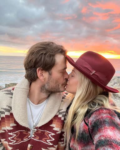 <p>Mira Sorvino Instagram</p> Christopher Backus and Mira Sorvino share a kiss with a sunset behind them.