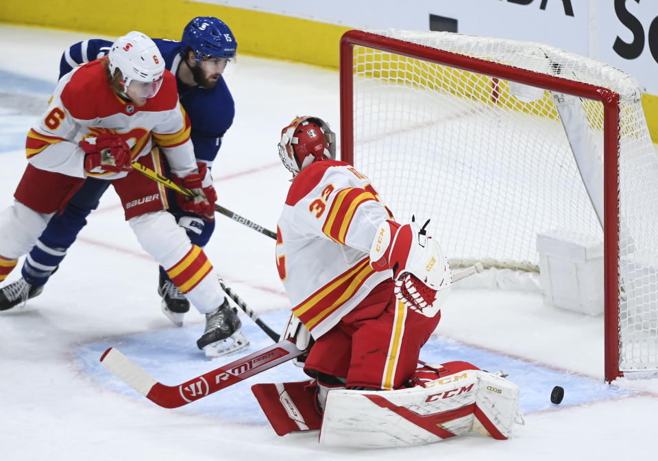 Calgary Flames goaltender David Rittich (33) makes a save but loses sight of the puck as Toronto Maple Leafs center Alexander Kerfoot (15) and Flames defenceman Juuso Valimaki (6) look on during the second period of an NHL hockey game in Toronto on Monday, Feb. 22, 2021. (Nathan Denette/The Canadian Press via AP)