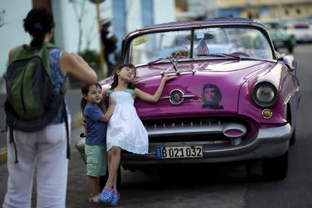 Young U.S. visitors pose for a photograph next to a vintage car in Havana March 16, 2016. REUTERS/Ueslei Marcelino