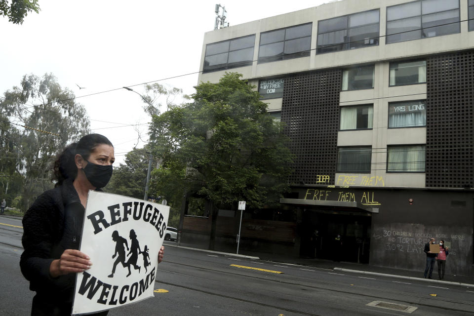 A protester holds a banner outside the Park Hotel calling for the release of refugees being detained inside the hotel in Melbourne, Australia, Saturday, Jan. 8, 2022. The world’s No. 1-ranked tennis player Novak Djokovic is also being held there after border officials canceled his visa last week over a vaccine requirement.(AP Photo/Hamish Blair)