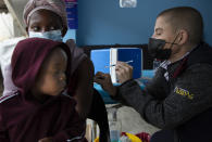 A woman, with her baby on her lap, gets vaccinated against COVID-19 at a site near Johannesburg, Wednesday, Dec. 8, 2021. Omicron cases have been confirmed in at least nine African countries, with South Africa remaining the epicenter, with officials reporting that initial cases appear to be mild.(AP Photo/Denis Farrell)