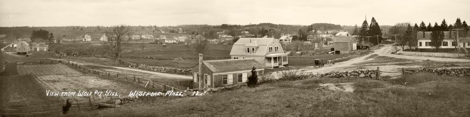 A view from Wolf Pit Hill looking west to Drift Road at the Head of Westport. In the far distance stands the Bell School and houses lining Drift Road. The Wolf Pit School (built in 1833) with its wide white shutters appears in the center foreground, close to the gambrel-roofed house built by W. F. King. On the far right stands the home of Dr. Tupper, who cared for seriously ill patients. Several buildings stand on the west landing across the river. Look closely to find a ladder leaning against a tree and the horse and buggy, probably belonging to the photographer.