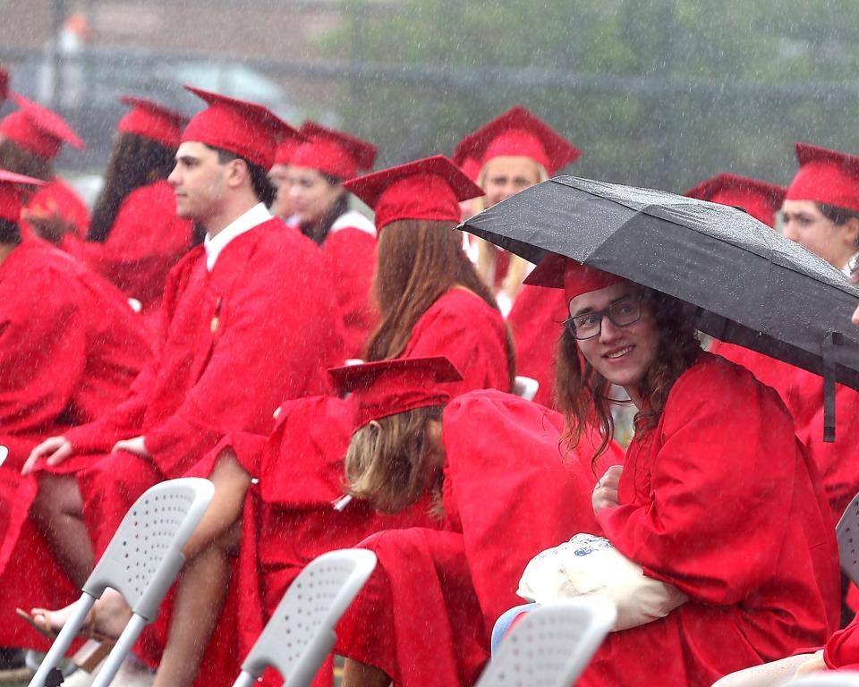 Hingham High senior Sean Shubin takes cover underneath an umbrella during a quick deluge during Hingham High’s graduation ceremony for the Class of 2023 on Saturday, June 3, 2023. Hingham High graduated 318 seniors. 