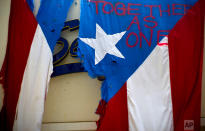 <p>A damaged Puerto Rican national flag spray painted with the words “Together as One” hangs from the facade of a business, in San Juan, Puerto Rico. The relief effort from Hurricane Maria in Puerto Rico has so far been concentrated largely in San Juan, and many outside the capital say they’ve received little or no help. (AP Photo/Ramon Espinosa) </p>