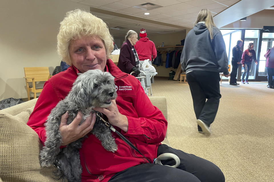 Linda Blackmore, executive director of the American Red Cross Minnesota Dakotas Region chapter, holds a small gray dog while waiting with residents at Unity Christian Reformed Church in Prinsburg, Minn., hours after a train derailed near their homes in Raymond, Minn., Thursday, March 30, 2023. The train was hauling ethanol and corn syrup and caught fire that morning, prompting officials to order hundreds of residents to evacuate. (AP Photo/Trisha Ahmed)