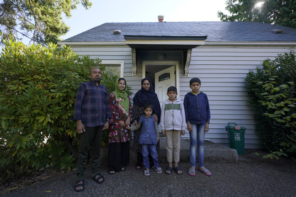 Abdul, left, who worked as a mechanic before he left Kabul, Afghanistan with his family about a month ago, poses for a photo, Thursday, Sept. 16, 2021, with his family in front of a rental house where they have been provided a place to stay in Seattle. The home is owned by Thuy Do, who was nine years old when her family arrived in the United States from Vietnam in the 1980s. Now Do and her husband have offered their vacant rental home to refugee resettlement groups to house newly arriving Afghans in need of a place to stay. (AP Photo/Ted S. Warren)