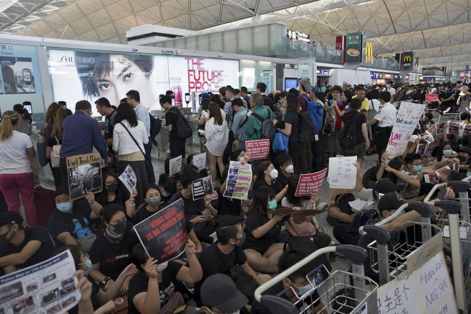 Travelers walk past as protesters hold a sit-in rally near the departure gate of the Hong Kong International Airport in Hong Kong, Tuesday, Aug. 13, 2019. (Photo: Vincent Thian/AP)