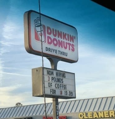 sign reading now hiring 3 pounds of coffee for $19.99 below a Dunkin' Donuts logo