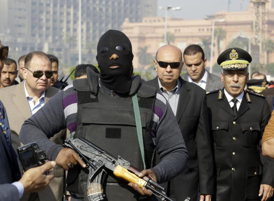 FILE - In this Saturday, Jan. 25, 2014 file photo, Egyptian masked policeman guards Cairo's state security chief, Osama al-Saghir, third right, as he visits Tahrir Square, the epicenter of the 2011 uprising, in Cairo, Egypt. On Tuesday, Feb. 11, 2014, the third anniversary of the day Hosni Mubarak stepped down as Egypt’s president after an 18-day uprising, the government blocked access to Tahrir Square and letters emerged from activists reporting that they have been beaten and subjected to other abuses by police after being arrested in a string of protests in late January. (AP Photo/Amr Nabil, File)