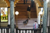 Deputy State Fire Marshal Kayla Riggs follows the agency's explosive detection dog, "Ringo," as he walks down the steps of the third floor at the Capitol in Jackson, Miss., Thursday, Jan. 14, 2021. With the FBI warning of potential violence at all state capitols Sunday, Jan. 17, the ornate halls of government and symbols of democracy looked more like heavily guarded U.S. embassies in war-torn countries. (AP Photo/Rogelio V. Solis)