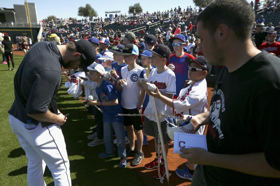 Cleveland Indians' Mike Freeman, left, signs autographs for fans as a Goodyear Stadium employee holds a container of pens and autograph cards prior to the team's spring training baseball game against the Chicago Cubs on Saturday, March 7, 2020, in Goodyear, Ariz. The stadium offered the items for players to sign autographs as a precaution for the coronavirus. (AP Photo/Ross D. Franklin)