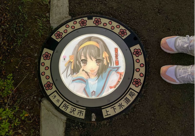 A passerby stands next to an illuminated manhole cover with designs of popular animation character from 'The Melancholy of Haruhi Suzumiya', on the street in Tokorozawa, near Tokyo