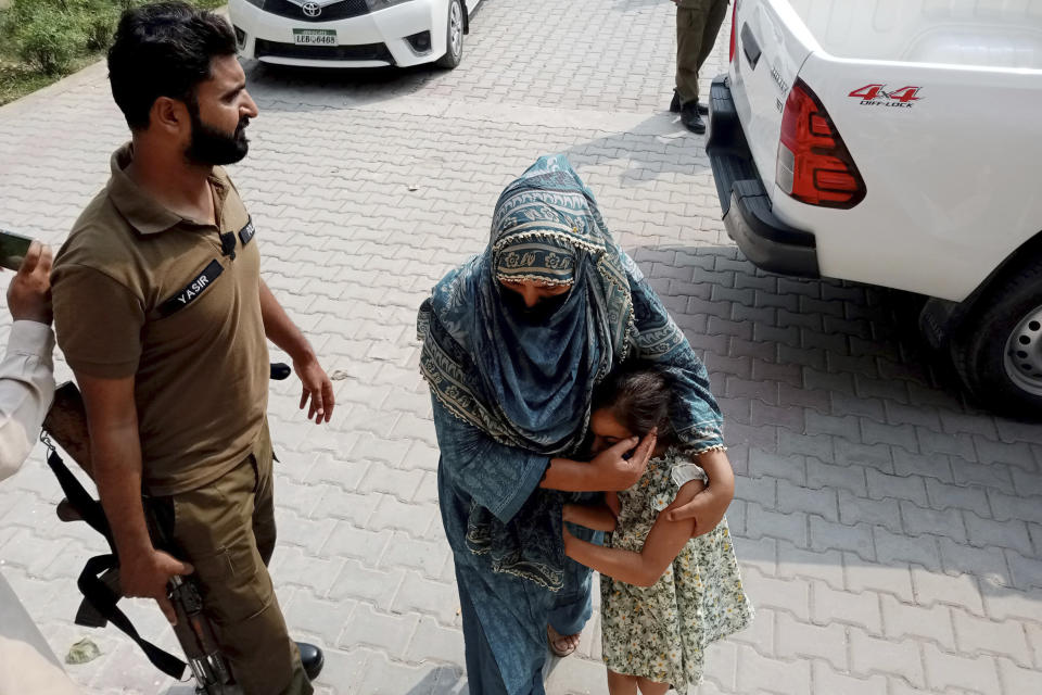Police officers escort a relative and a child of a couple wanted by British police in connection with last month's death of their 10-year-old daughter on the outskirts of London, to appear them in a court in Jhelum, about 175 kilometres (110 miles) northwest of Lahore in central Pakistan, Tuesday, Sept. 12, 2023. A Pakistani court ordered the five siblings of a 10-year-old girl who was found dead at her British home put in the custody of a children's protection center after they were recovered following a notice from Interpol. The police are continuing their search for the girl’s father and stepmother in connection with her death. (AP Photo/Tahir Mahmood)