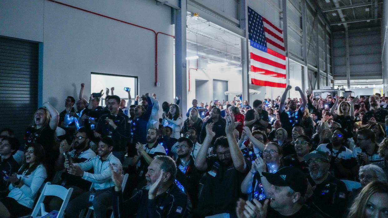  A crowd of people in a warehouse cheer in front of a large american flag. 