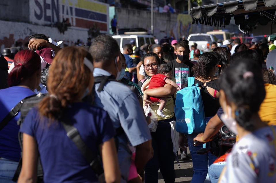 A woman walks with a baby in her arms on a crowed street in Caracas, Venezuela, Tuesday, Nov 30, 2021. Venezuela's Supreme Court of Justice ordered a repeat election for the governorship of Barinas, the home state of the late President Hugo Chávez, excluding the opposition candidate Adolfo Superlano, who was emerging as the winner of the Nov. 21, regional election. (AP Photo/Ariana Cubillos)