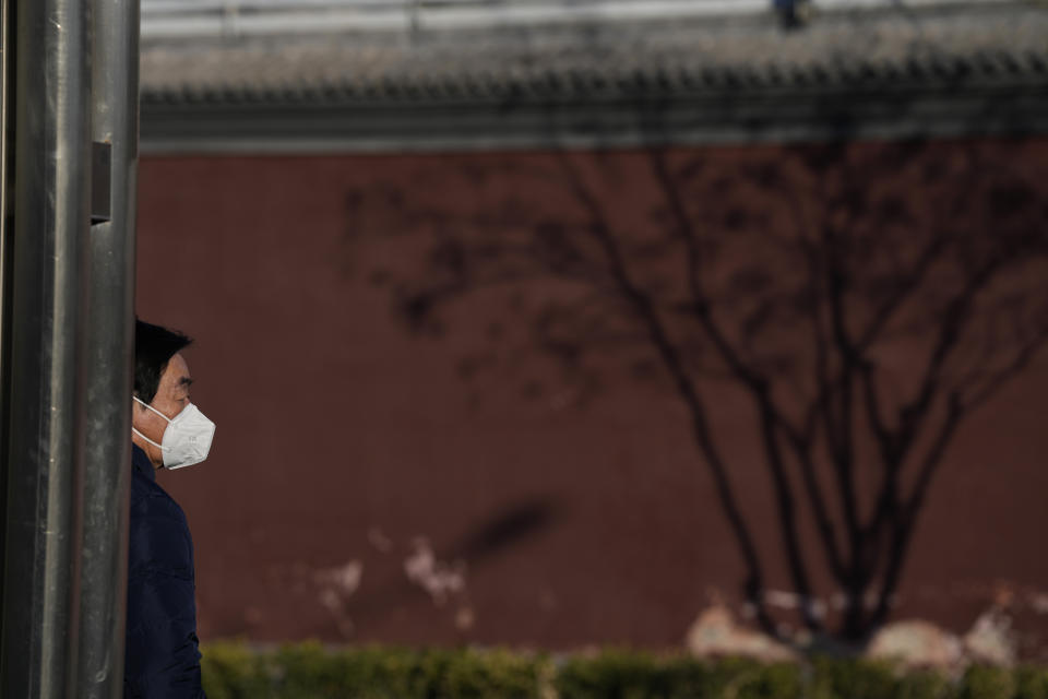 A resident wears a mask as he stands near the shadow of a tree on the maroon walls of the Lama Temple in Beijing, Tuesday, Dec. 27, 2022. Companies welcomed China's decision to end quarantines for travelers from abroad as an important step to revive slumping business activity while Japan on Tuesday announced restrictions on visitors from the country as infections surge. (AP Photo/Ng Han Guan)