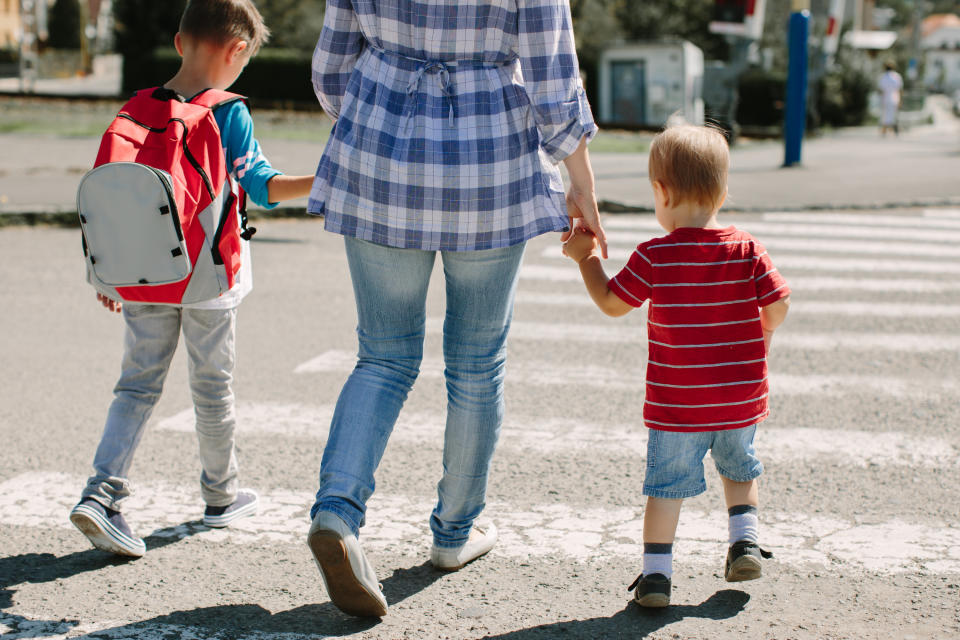 A woman holds her kids' hands while they cross the street together