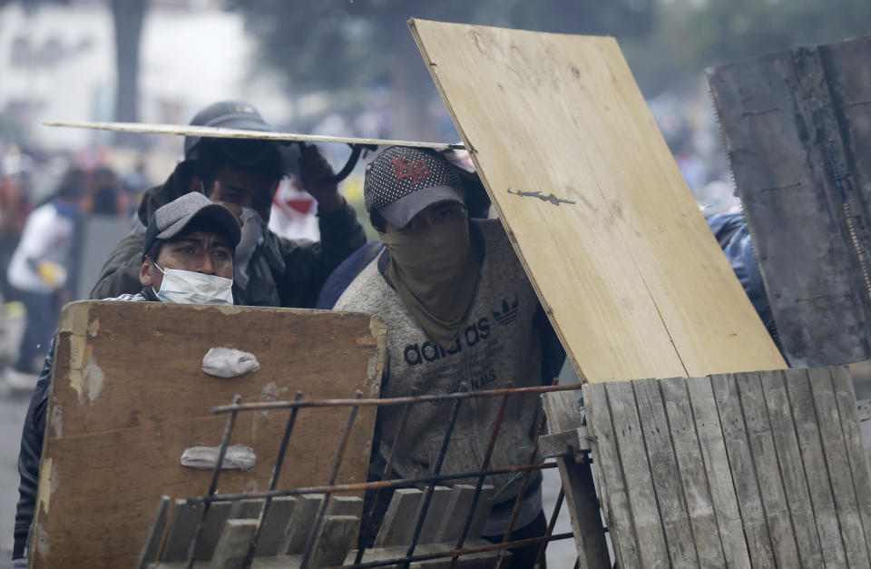 Anti-government demonstrators take cover behind a barricade during clashes with police in Quito, Ecuador, Saturday, Oct. 12, 2019. Protests, which began when President Lenin Moreno's decision to cut subsidies led to a sharp increase in fuel prices, have persisted for days. (AP Photo/Fernando Vergara)