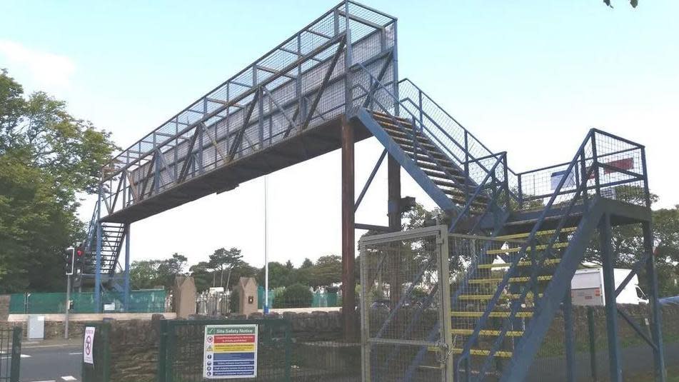 A metal footbridge over a road with yellow steps to the top