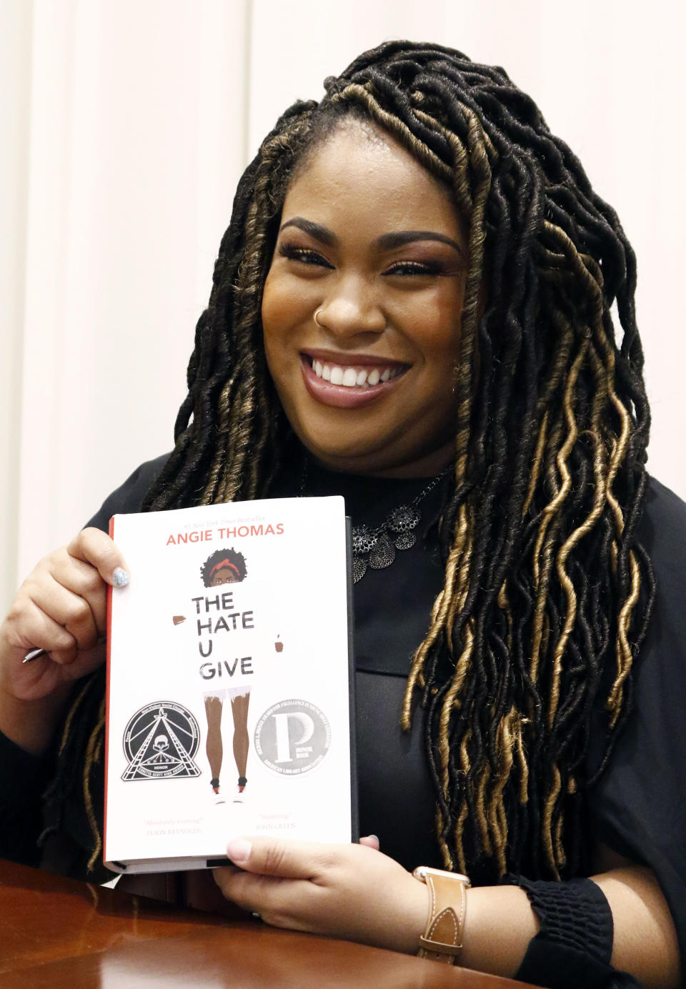 FILE - In this Oct. 10, 2018 photograph, author Angie Thomas holds a copy of her novel, "The Hate U Give," at a book signing in Jackson, Miss. Thomas' best-selling novel about a black teen murdered by police was adapted into a feature film of the same name. (AP Photo/Rogelio V. Solis, File)