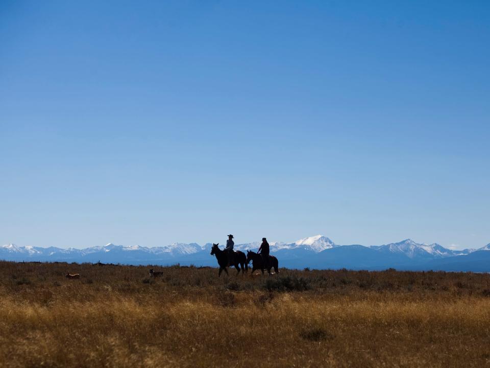 Two men, in silhouette, riding horseback, against backdrop of mountains