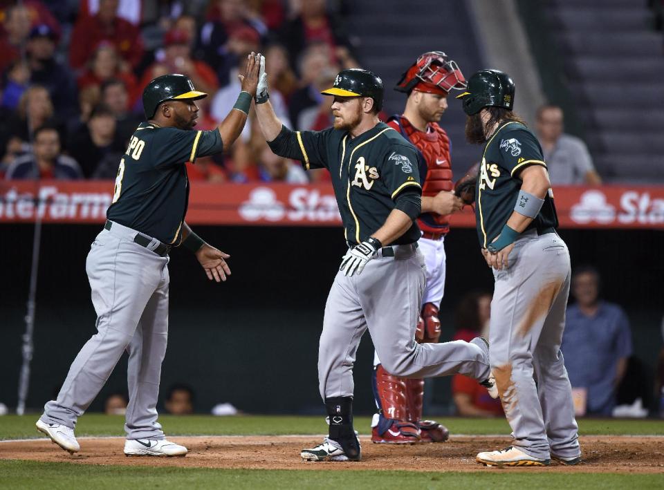 Oakland Athletics' Brandon Moss, second from left, is congratulated by Alberto Callaspo, left, and Derek Norris, right, after hitting a three-run home run, as Los Angeles Angels catcher Chris Iannetta stands behind them during the fourth inning of a baseball game, Wednesday, April 16, 2014, in Anaheim, Calif. (AP Photo/Mark J. Terrill)