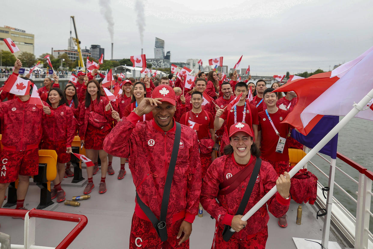 Canada's flagbearers Maude Charron, right, and Andre de Grasse, left, pose for photos on a boat with their team before the start of the opening ceremony. / Credit: Cao Can / AP