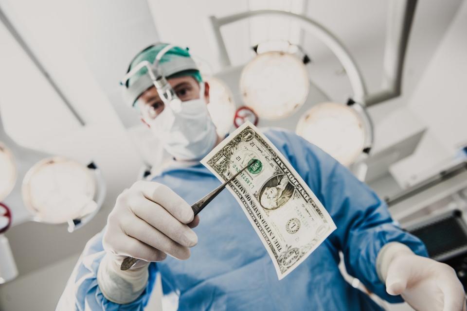 A surgeon holding a one dollar bill with surgical tweezers in an operating room. 