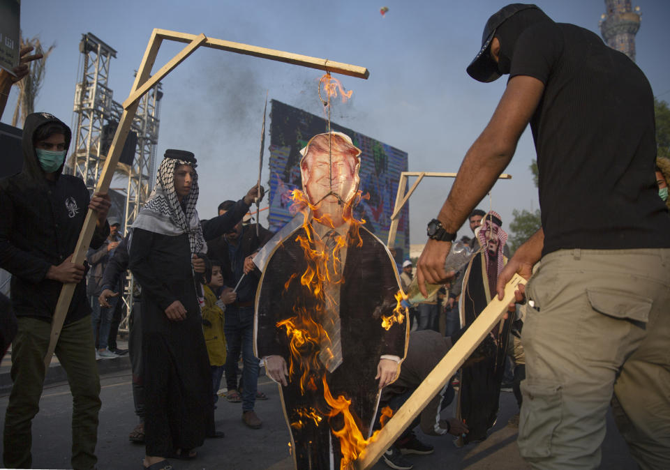 Protesters set on fire a cardboard cutout that depicts US President Donald Trump and hung to a gallows, during a rally for the Shiite group Asaib Ahl al-Haq, in Baghdad, Iraq, Saturday, Dec. 14, 2019. (AP Photo/Nasser Nasser)