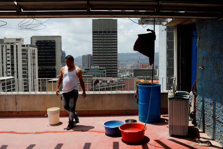 Wilson Hernandez stands next to buckets of water on the roof of an apartment block in Caracas, Venezuela, March 17, 2019. REUTERS/Carlos Jasso