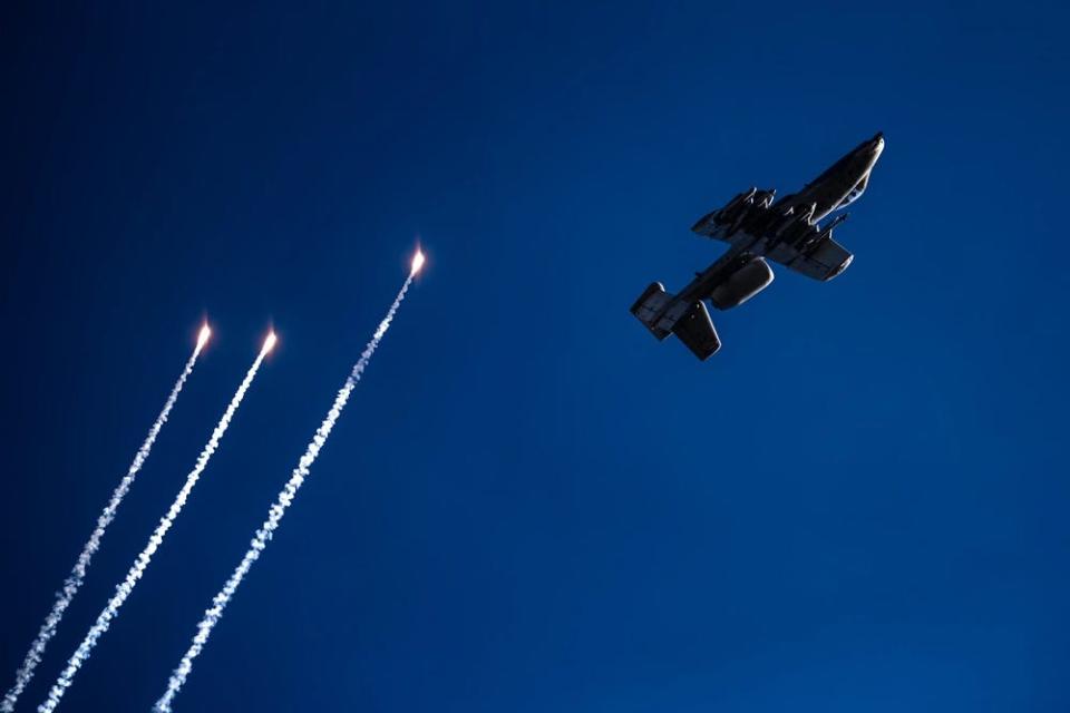 a gray fighter jet flies in the sky next to three flares