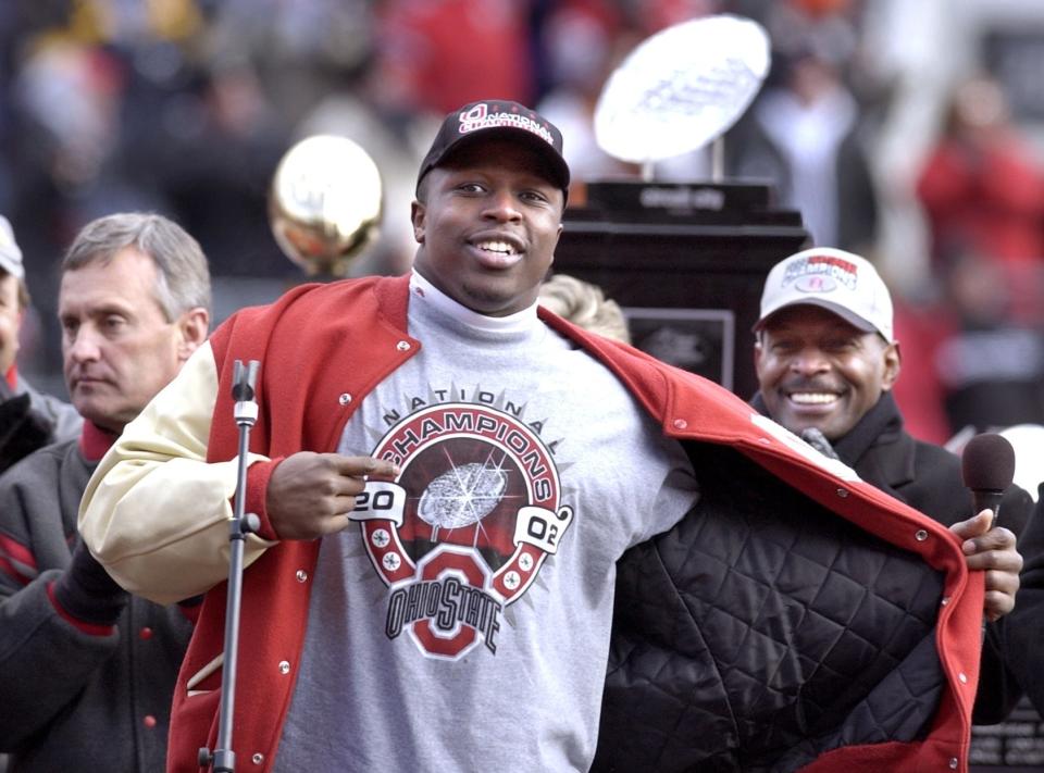 Mike Doss shows off his national champions t-shirt at the Ohio Stadium during the celebration. At left is head coach Jim Tressel and at right is former Ohio State two time Heisman Trophy winner Archie Griffin. The national championship trophy is in the background.