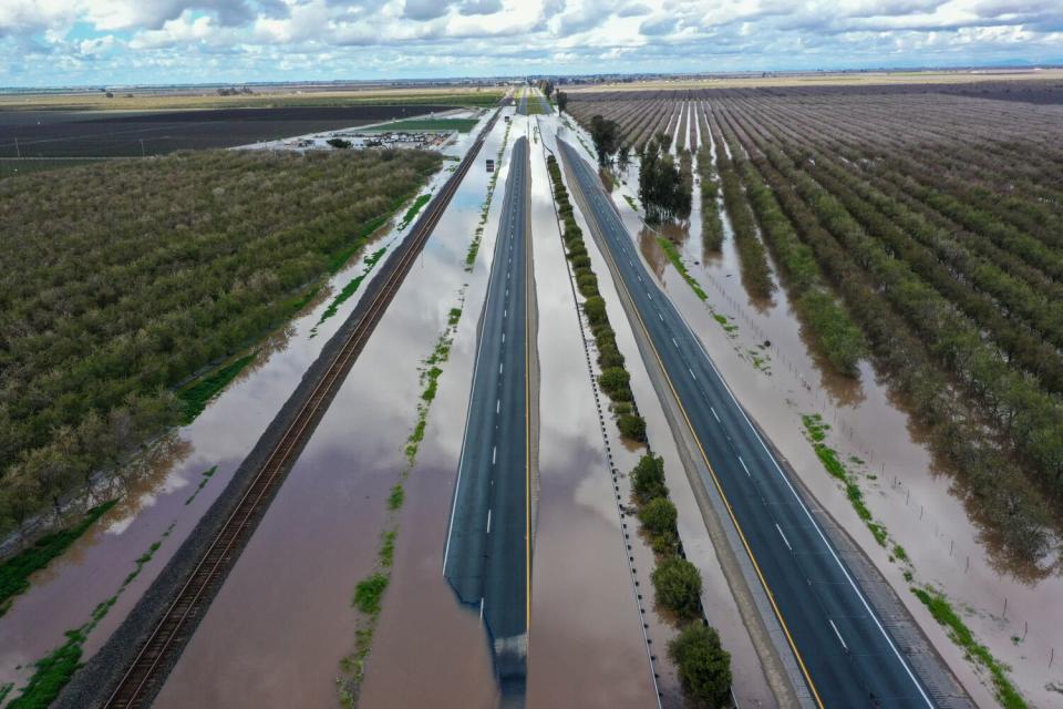 Both sides of Highway 99 are partially submerged in floodwaters and no cars are on it.