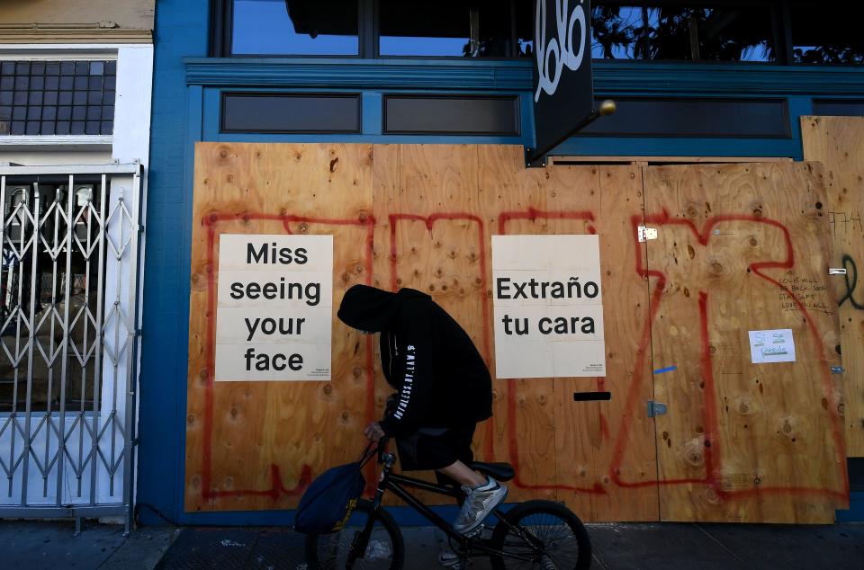 A man in a face mask rides his bike past a sign posted on a boarded up restaurant in San Francisco, California on April, 1, 2020, during the novel coronavirus outbreak. - The US death toll from the coronavirus pandemic topped 5,000 late on April 1, according to a running tally from Johns Hopkins University. (Photo by Josh Edelson / AFP) (Photo by JOSH EDELSON/AFP via Getty Images)