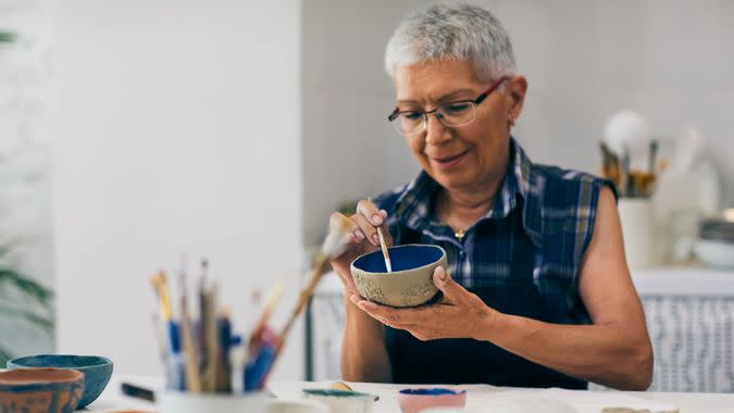 Senior woman decorating bowl made of clay on ceramics workshop.