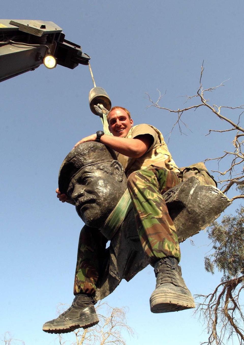 Lance Cpl. Graeme Church sits on the head of a 17-foot tall statue of Saddam Hussein that was toppled by Royal Electrical Mechanical Engineers 25 Armored Engineer squadron, 2RTR battle group, in Az Zubaya, Iraq, on April 1, 2003.