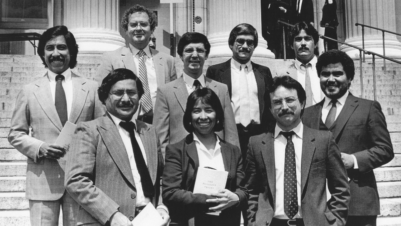 Several people in business suits smiling while standing on stairs in front of columns.