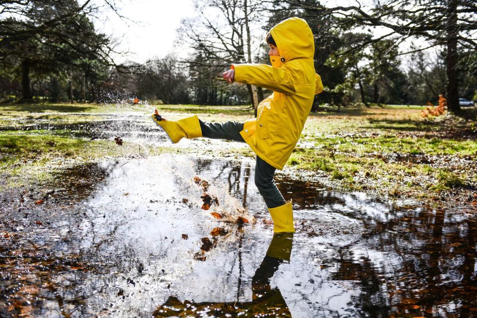 summer activities boy in yellow raincoat splashing in park puddle