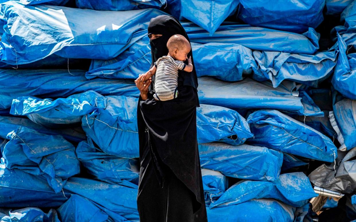 A woman walks carrying an infant at al-Hol camp for families with connections to the Islamic State - AFP