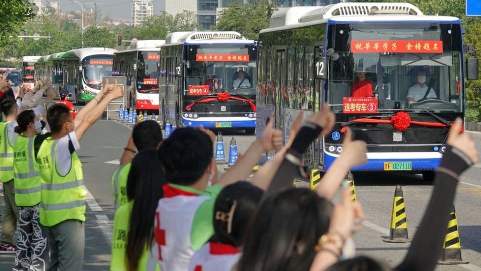 People gesture to buses transferring students to attend the National College Entrance Examination (NCEE), known as 