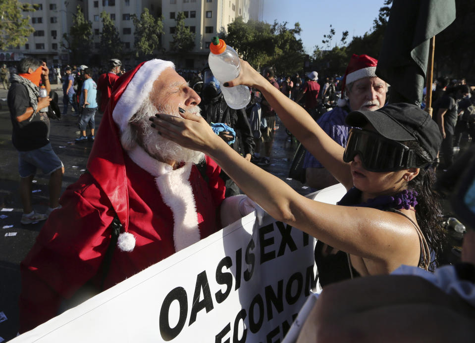 An anti-government demonstrator dressed in a Santa Clause costume has his face rinsed with a mixture of water and baking soda to relieve the effect of teargas during clashes with the police in Santiago, Chile, Friday, Dec. 20, 2019. Chile marks a second full month of unprecedented social revolt that has not only altered the country's political landscape but also prompted a referendum on reforming the country's dictatorship-era. (AP Photo/Fernando Llano)