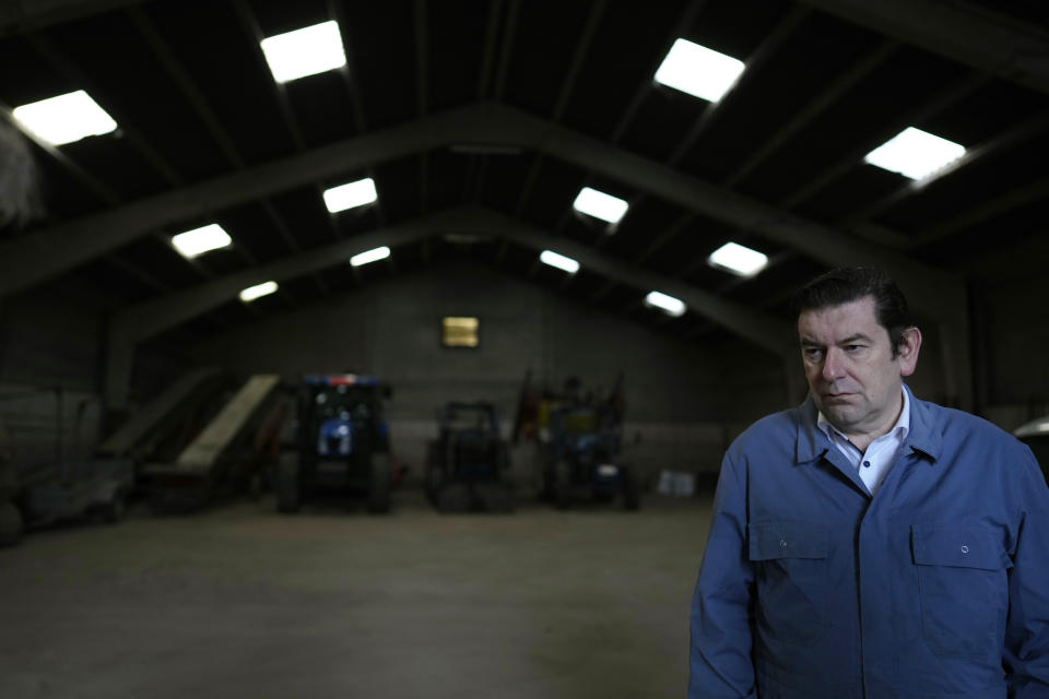 Bart Dochy stands in front of tractors in a barn at his family farm in Ledegem, Belgium, Tuesday, Feb. 13, 2024. After dealing with hectacres of fields and barns full of animals Dochy just as handily steps into a three-piece suit to pick up his job as mayor of this farming community in Landegem. (AP Photo/Virginia Mayo)