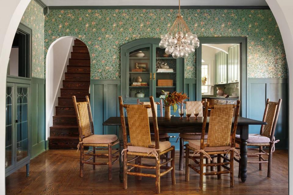 a dining room with green blue wainscoting and wallpaper above, dining table surrounded by cabin style chairs