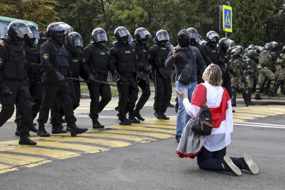 FILE - In this Sunday, Sept. 13, 2020 file photo, a woman covered by an old Belarusian national flag kneels in front of a riot police line as they block Belarusian opposition supporters rally protesting the official presidential election results in Minsk, Belarus. Belarus President Alexander Lukashenko has relied on massive arrests and intimidation tactics to hold on to power despite nearly three months of protests sparked by his re-election to a sixth term, but continuing protests have cast an unprecedented challenge to his 26-year rule. (TUT.by via AP, File)