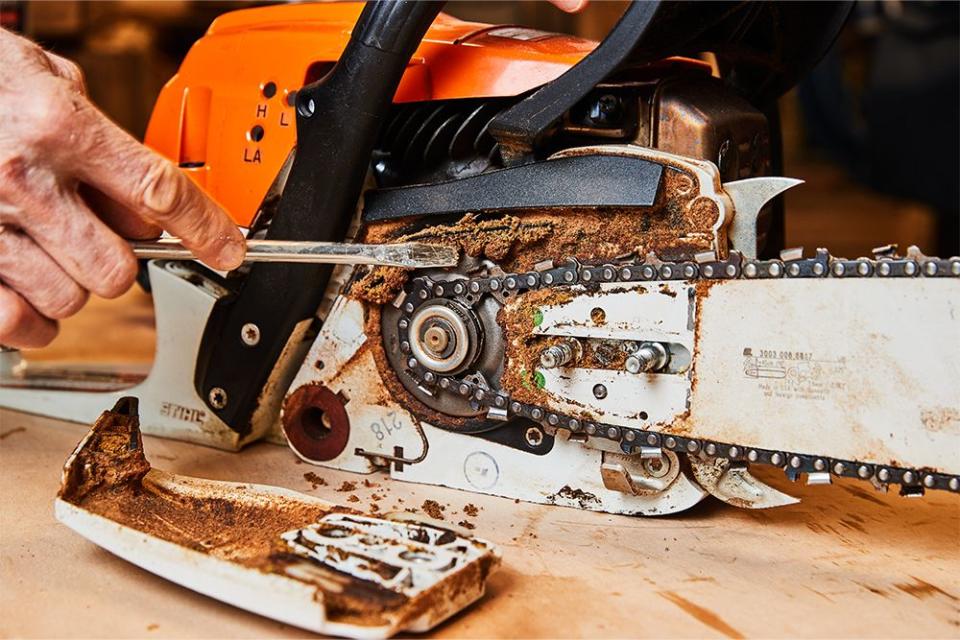 a person cleaning out built up wood chips, oil, and dirt from a chainsaw