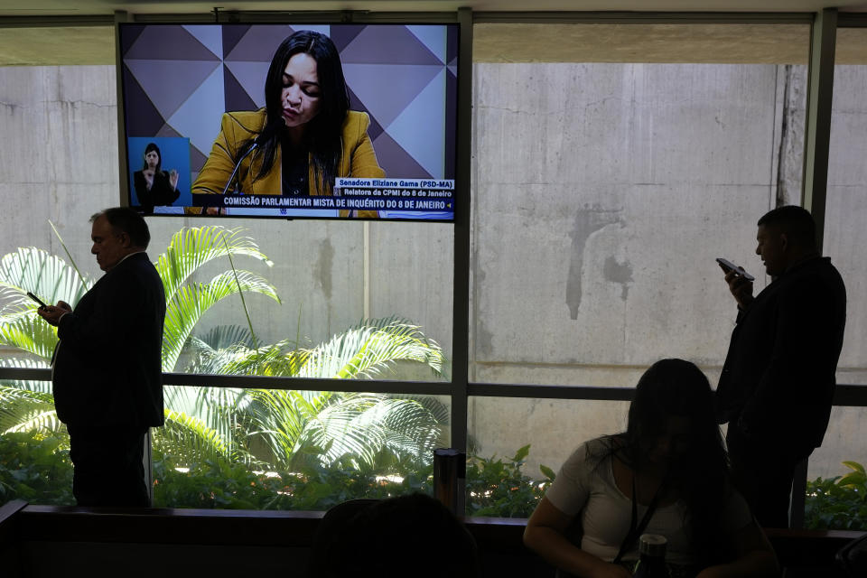 Journalists stand in the back of the room where Senator Eliziane Gama, shown on screen, reads her report and recommendation before the Parliamentary Inquiry Committee that is investigating the Jan. 8 uprising in Brazil's capital, at the Federal Senate in Brasilia, Brazil, Tuesday, Oct. 17, 2023. (AP Photo/Eraldo Peres)