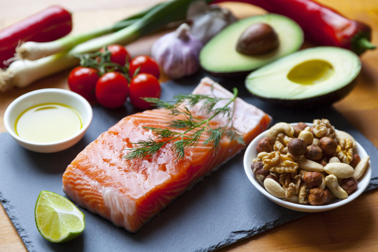 Table top still life of foods high in healthy fats such as Salmon, olive oil, nuts and avocados with vegetables and herbs.