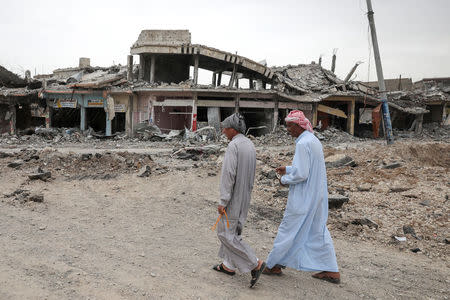 Displaced Iraqi men walk past damaged buildings as the battle between the Iraqi Counter Terrorism Service and Islamic State militants continues nearby, in western Mosul, Iraq, April 23, 2017. REUTERS/Marko Djurica